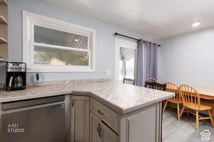 Kitchen featuring a stainless steel dishwasher, light-toned cabinetry, and patterned countertops