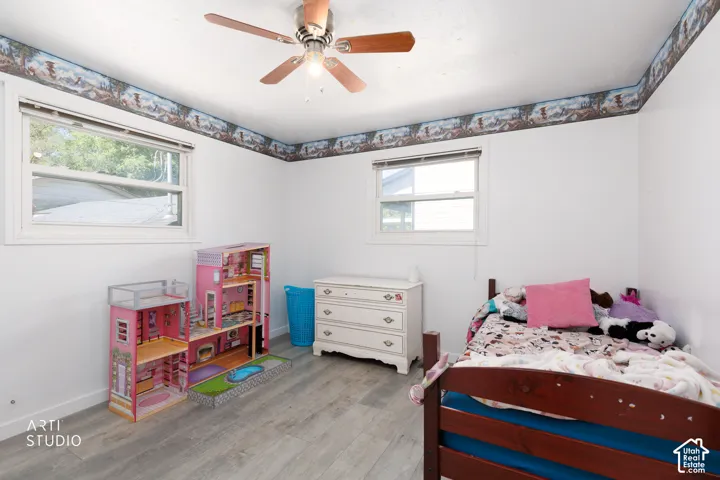 Light-toned wood-finish flooring, white walls, two windows with white trim, and a ceiling fan with integrated lighting