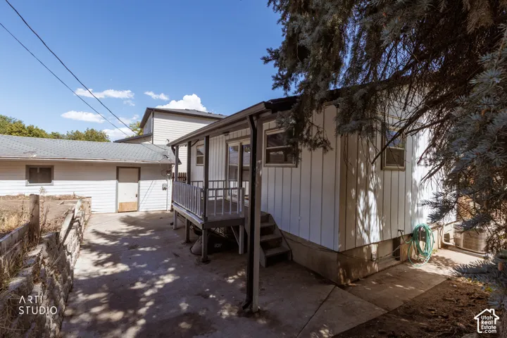 Rear exterior featuring a covered porch with railings, concrete patio, and an outbuilding with a single entry door