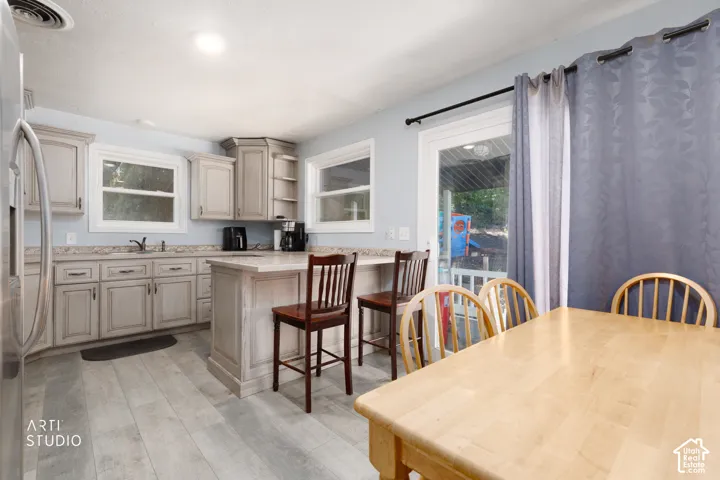 Light-toned wood-finish flooring, light-colored cabinetry, remodeled kitchen built-in kitchen island, stainless steel refrigerator, and glass sliding door