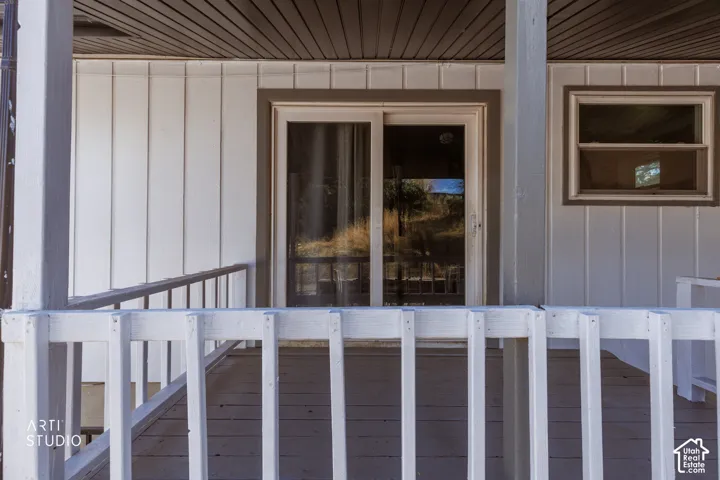 Exterior featuring vertical white siding, a sliding glass door, a single pane window, and a wood-finish porch with white railings