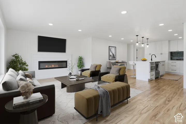 Open-concept living space featuring wood-finish flooring, a linear fireplace with a shiplap surround, recessed lighting, and a kitchen island with pendant lights. Virtual staging in this photo.