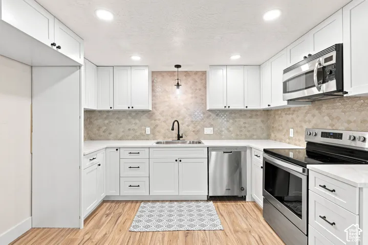 Contemporary kitchen featuring white shaker cabinetry, stainless steel appliances, light-toned hexagon tile backsplash, and wood-finish flooring