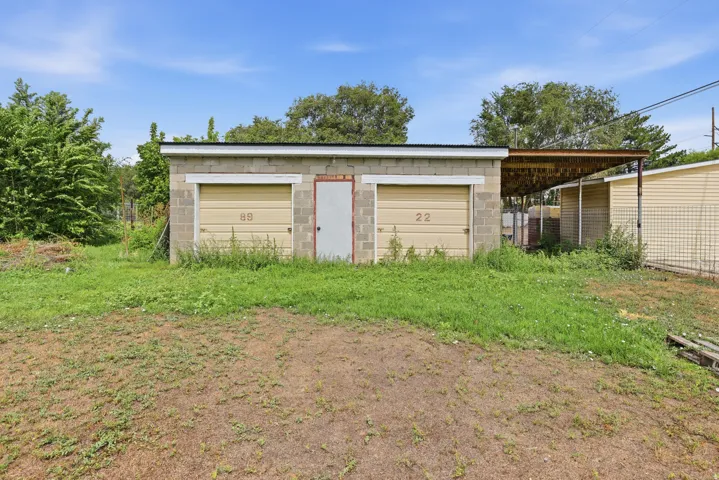 Block construction outbuilding featuring two garage doors, an exterior side door, and an attached covered carport