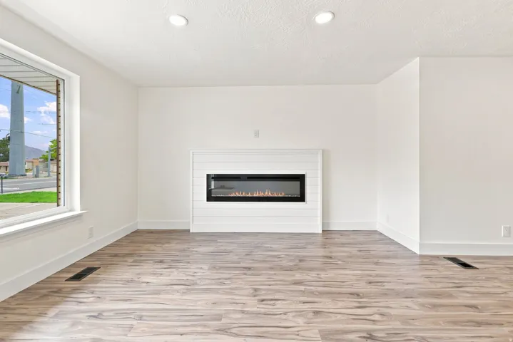 Wood-finish flooring, recessed lighting, and a modern linear electric fireplace with a shiplap surround