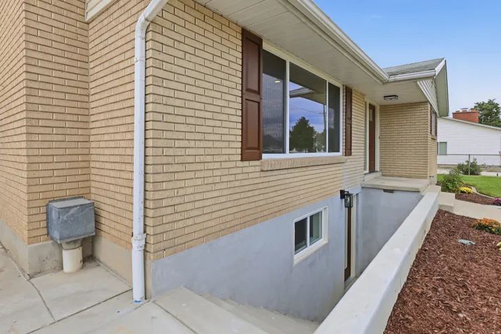 Exterior featuring brick siding, white-framed windows with brown shutters. Basement entry prior to handrail installation.