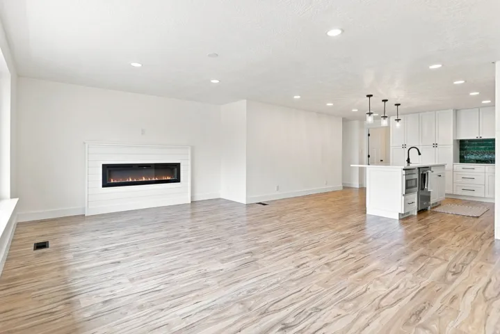 Open-concept living space featuring wood-finish flooring, a contemporary fireplace with shiplap surround, and recessed lighting