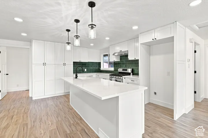 White cabinetry, quartz countertops, central island, green subway tile backsplash, and wood-finish flooring
