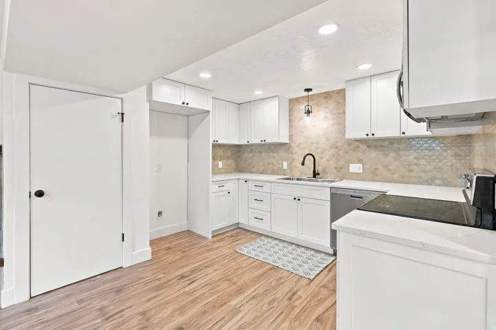White cabinetry, light wood-finish flooring, light-colored backsplash, light countertops, and recessed lighting