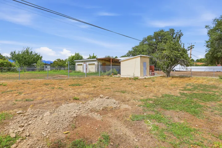 Expansive lot featuring a chain-link fence, various outbuildings, and mature trees