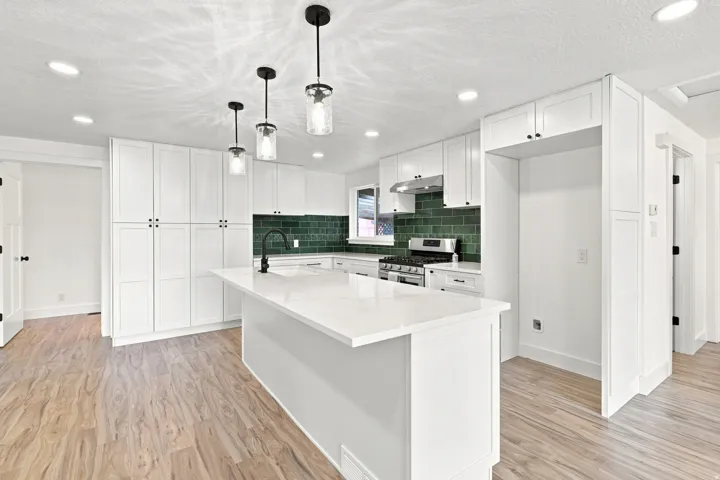 White cabinetry, quartz countertops, central island, green subway tile backsplash, and wood-finish flooring