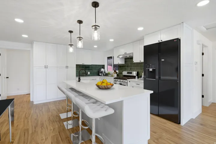 White cabinetry with dark hardware, wood-finish flooring, a kitchen island with a white countertop, recessed lighting, and dark pendant lights
