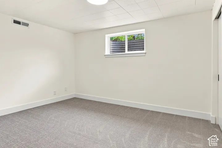 Neutral wall paint, gray patterned carpet, drop ceiling, and a single window