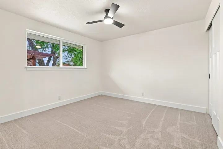 Neutral tone wall paint, light-colored carpet flooring, white window trim, white baseboards, and a modern ceiling fan with integrated lighting