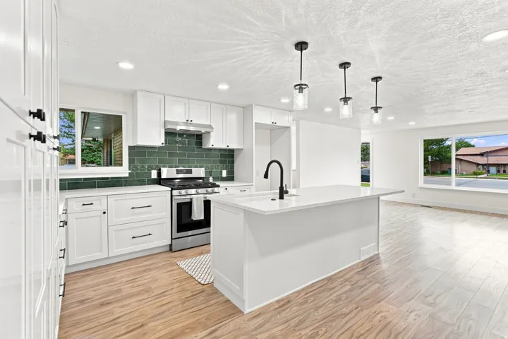 White shaker cabinetry, quartz countertops, stainless steel appliances, dark green subway tile backsplash, and wood-finish flooring