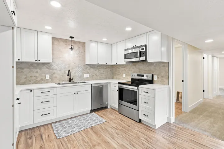 White cabinetry, stainless steel appliances, wood-finish flooring, recessed lighting, and a textured backsplash