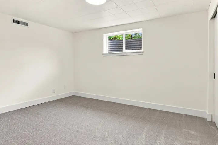 Neutral wall paint, gray patterned carpet, drop ceiling, and a single window