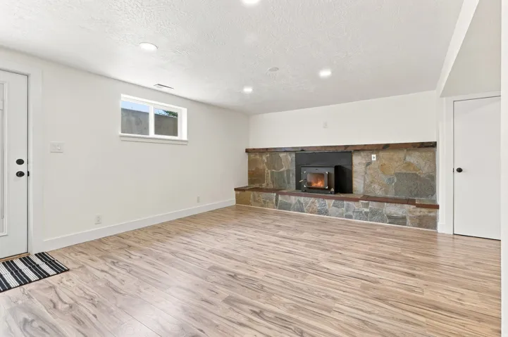 Wood-finish flooring, recessed lighting, and a stone-clad fireplace with a wood-burning insert
