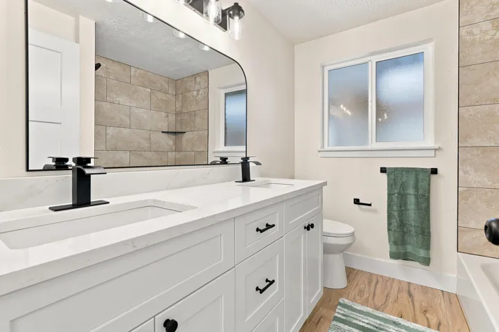 Full Bath with double vanity with integrated rectangular sinks, white cabinetry, matte black hardware, and a white countertop and bathtub shower