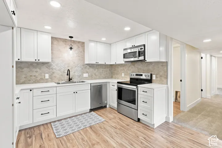 White cabinetry, stainless steel appliances, wood-finish flooring, recessed lighting, and a textured backsplash