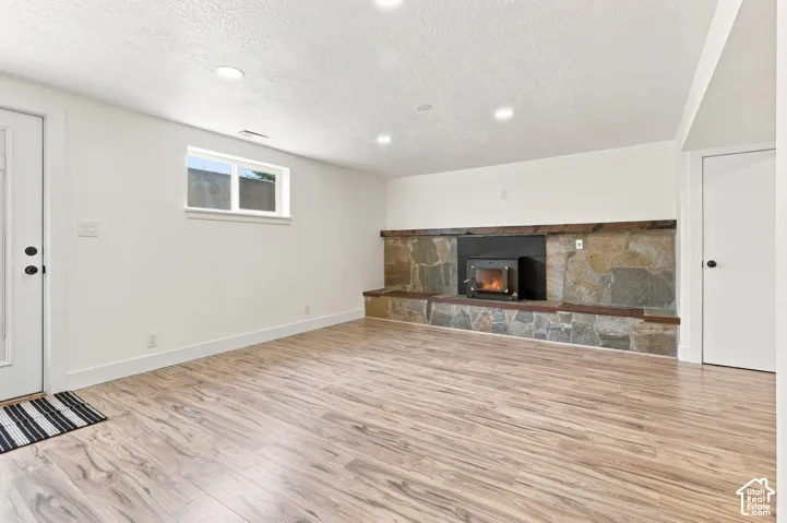 Wood-finish flooring, recessed lighting, and a stone-clad fireplace with a wood-burning insert. Staged fire in this photo.