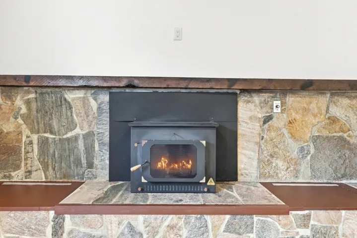 Wood-burning stove set within a stone-clad fireplace, featuring a raised stone hearth and integrated wood-finish benches