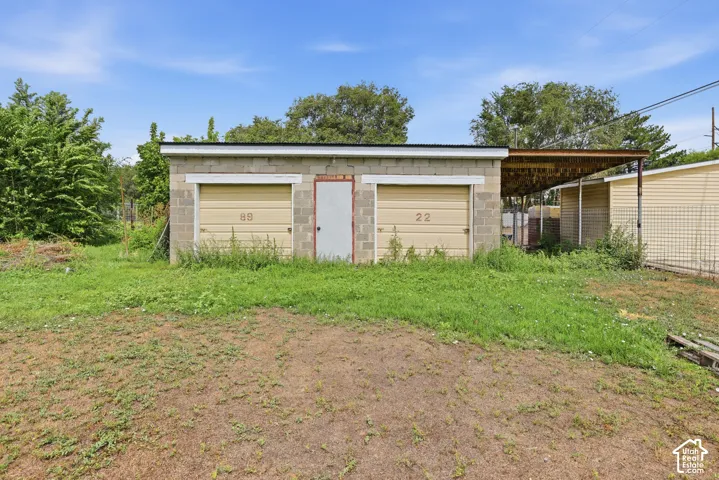 Block construction outbuilding featuring two garage doors, an exterior side door, and an attached covered carport