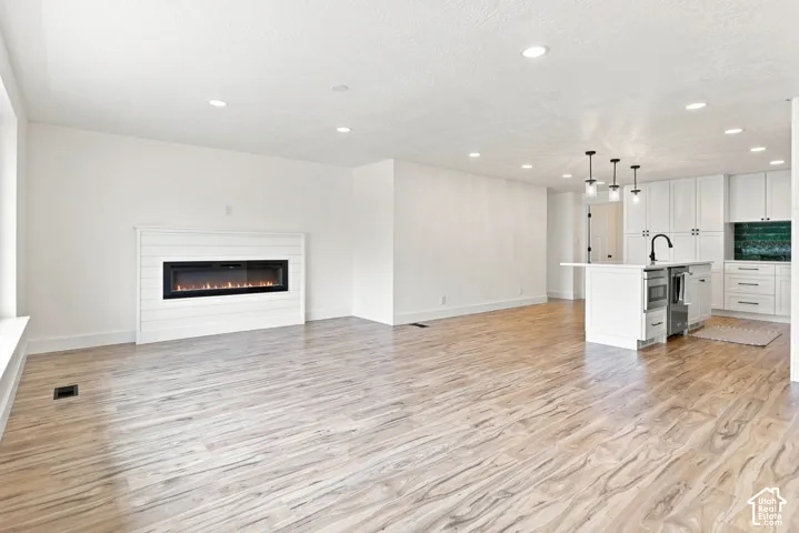 Open-concept living space featuring wood-finish flooring, a contemporary fireplace with shiplap surround, and recessed lighting.