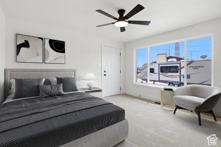 Master bedroom ceiling fan lighting, broad window, paneled door, and neutral wall color with plush carpet. Virtual staging in this photo.