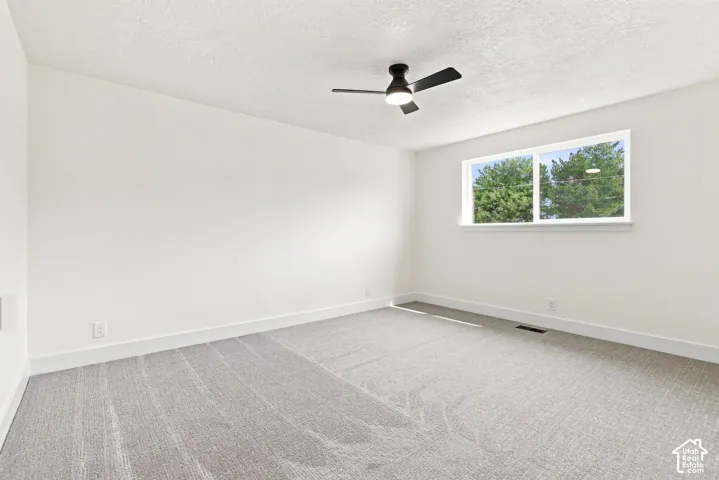 Spacious interior with neutral wall tones, light gray patterned carpeting, a large window, and a ceiling fan with integrated lighting