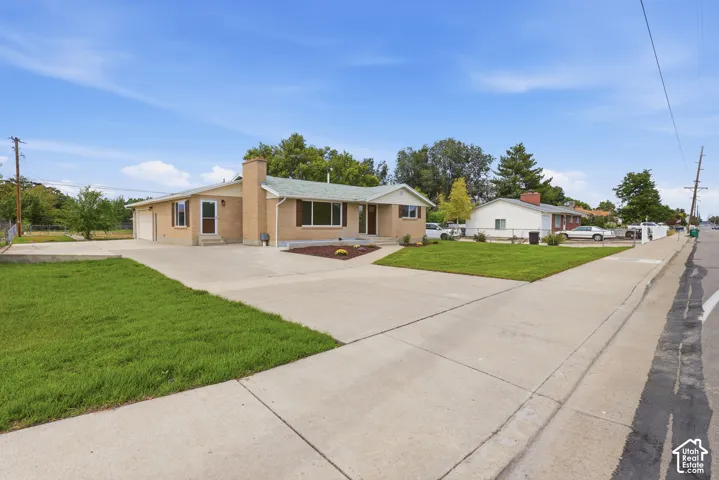 Brick exterior residence with a concrete driveway and sidewalk, featuring a landscaped front yard with grass and plantings