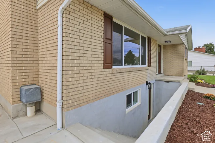 Exterior featuring brick siding, white-framed windows with brown shutters. Basement entry prior to handrail installation.