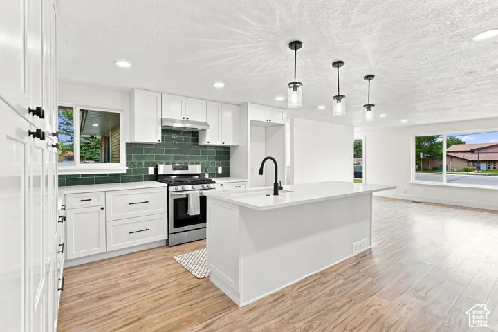 White shaker cabinetry, quartz countertops, stainless steel appliances, dark green subway tile backsplash, and wood-finish flooring