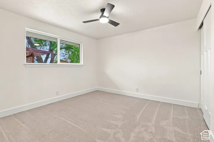 Neutral tone wall paint, light-colored carpet flooring, white window trim, white baseboards, and a modern ceiling fan with integrated lighting