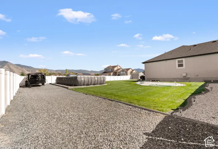 Expansive gravel driveway, white privacy fencing, manicured lawn, and a level property lot