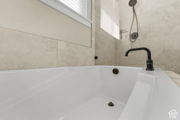 White soaking tub with matte black fixtures and a tile surround