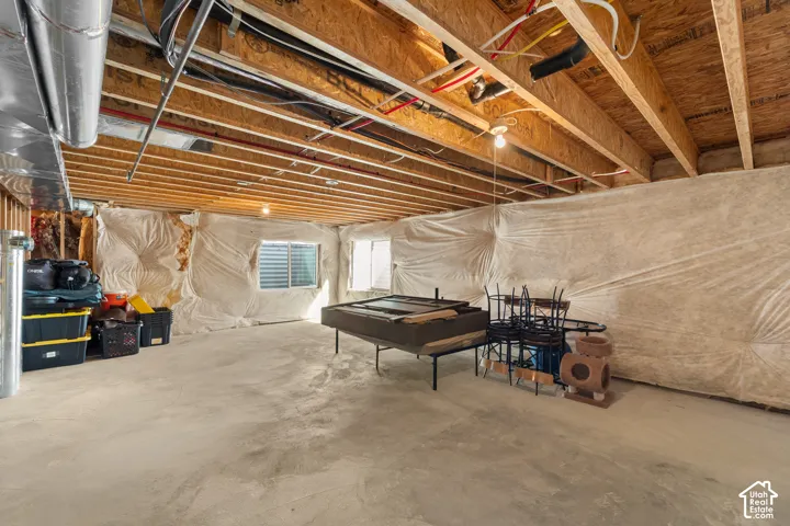 Unfinished basement featuring exposed wood joists, concrete flooring, and multiple egress windows