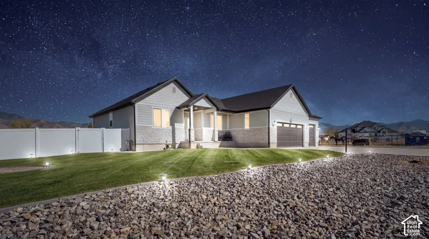 Home exterior featuring light gray siding, stone accents, a dark shingle roof, and a two-car garage