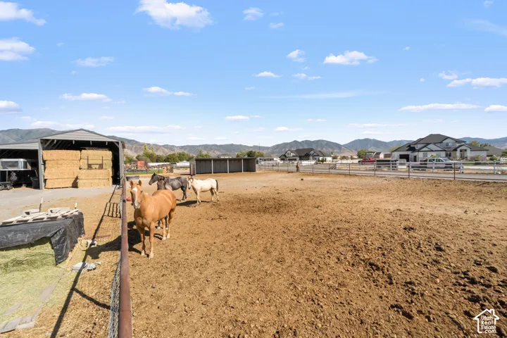 Expansive outdoor area featuring a large, fenced enclosure, a covered hay storage structure, and distant mountain scenery