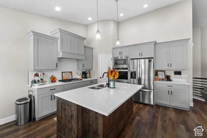 Kitchen featuring a center island with double basin sink, white countertops, gray cabinetry, stainless steel appliances, and wood-finish flooring