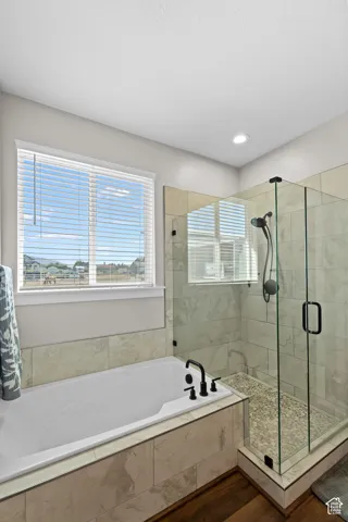 Built-in soaking tub with matte black fixtures, glass-enclosed shower with a pebble floor, and large format tile surrounds