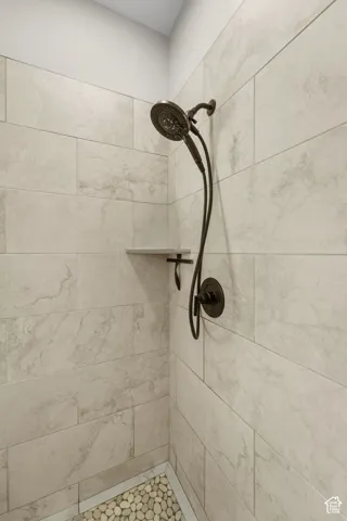 Shower stall with light-toned rectangular wall tiling, a built-in corner shelf, and a dark bronze showerhead with an attached handheld sprayer