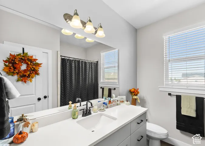 Vanity with integrated sink and chrome faucet, large wall-mounted mirror, multiple-bulb vanity light fixture, and window with blinds