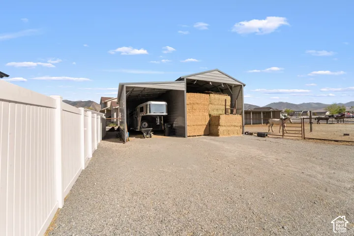 Gravel driveway featuring a white privacy fence, an open-sided metal structure, and a fenced animal enclosure