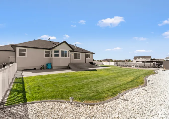 Expansive backyard featuring a manicured lawn, white privacy fencing, a concrete patio, and a dedicated gravel area