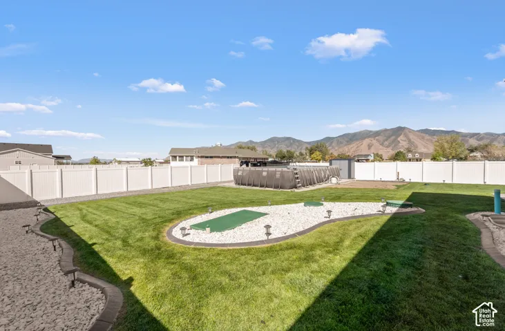 Expansive landscaped backyard with a manicured lawn, white vinyl fencing, a putting green, and mountain backdrop