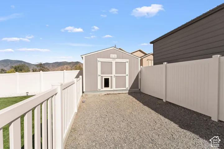 Detached storage shed, gravel ground cover, white vinyl fencing, and mountain backdrop
