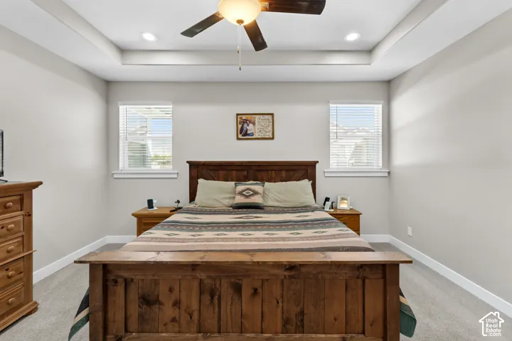 Tray ceiling with recessed lighting and a ceiling fan, two windows with blinds, and light gray wall paint