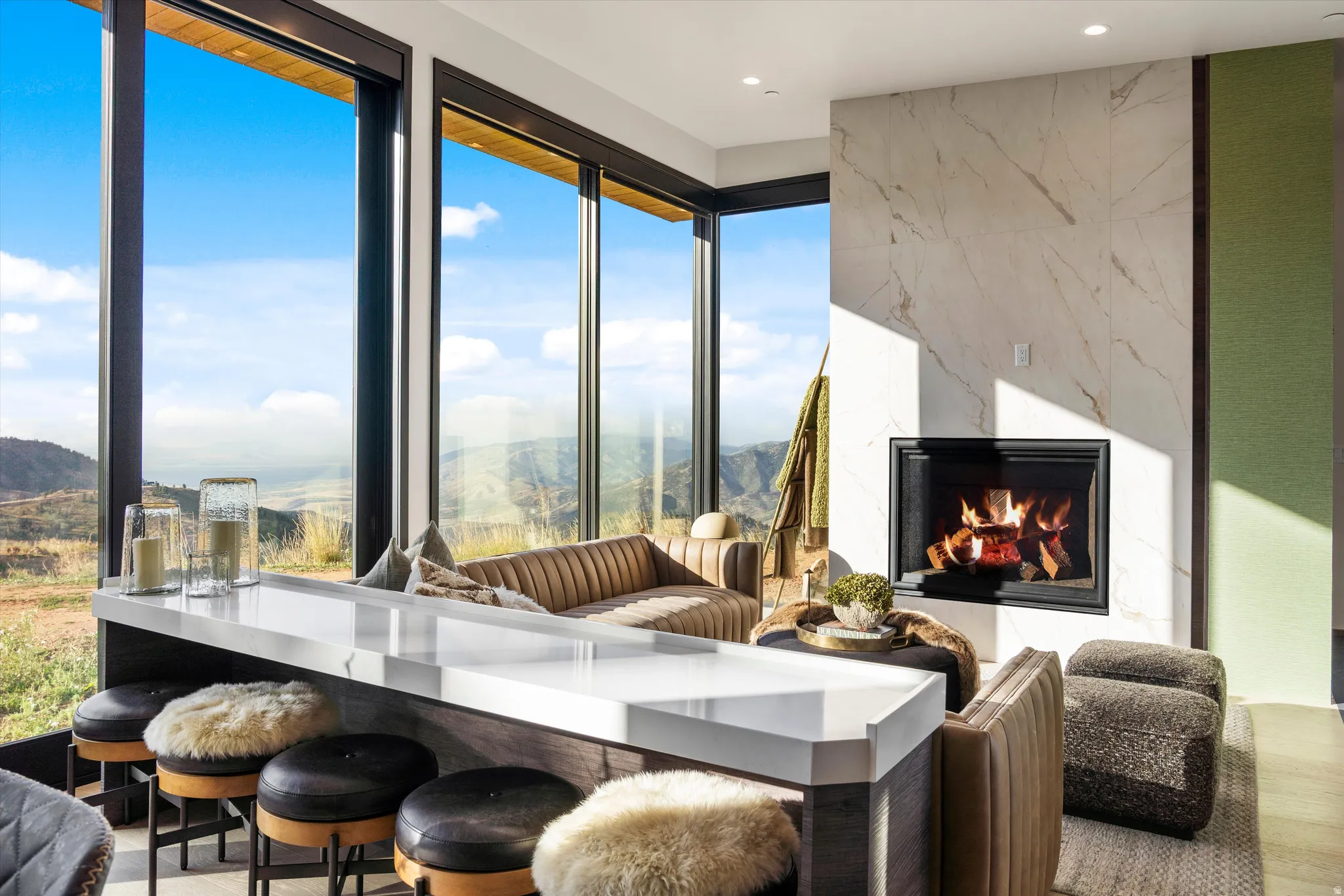 Floor-to-ceiling windows, a built-in bar, a modern fireplace with a stone-look surround, and wood-finish flooring
