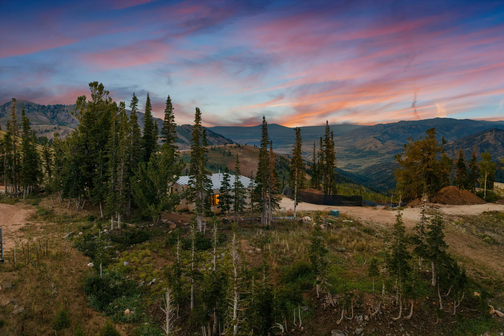 Expansive mountain property featuring mature coniferous and deciduous trees, natural terrain with rolling hillsides, and panoramic sunset vistas across the valley landscape